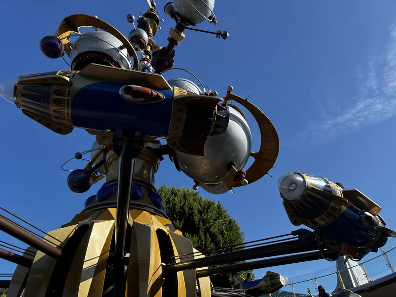 Gold and blue rocket arms of the Astro Orbitor ride seen from below against a deep blue sky