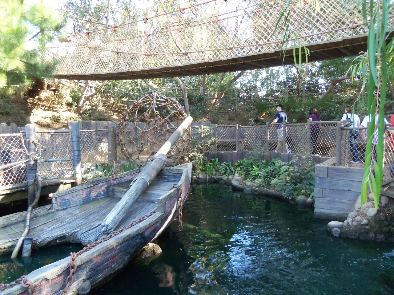 A wooden canoe beneath rope bridges and green trees