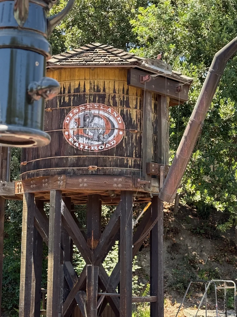 Weathered wooden Disneyland Railroad water tower surrounded by green trees
