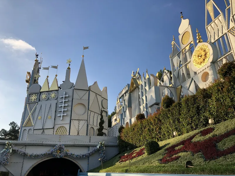 White spires and clock face of the it's a small world facade above a flower-bed lawn