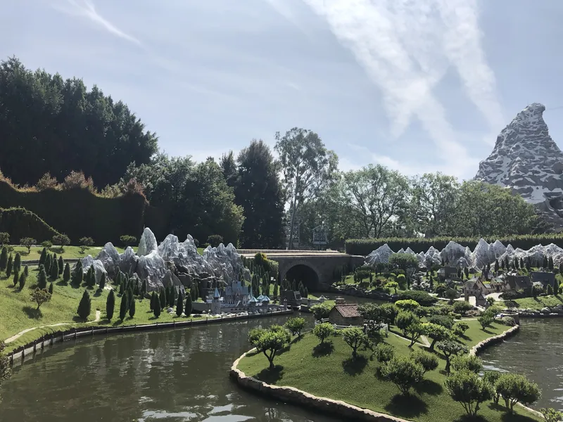Miniature hills, trees and a stone bridge along the Storybook Land canal, with the Matterhorn rising behind